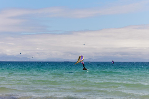 Kitesurfeur et amateurs de planche à voile près du parc de vacances TAIGA Tarifa en Andalousie, Espagne, montagnes en fond.
