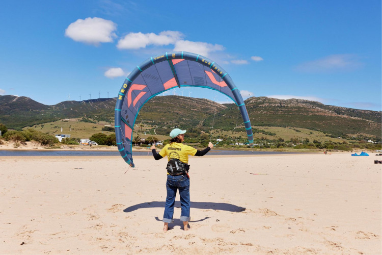 Instructeur met een vlieger op het strand bij TAIGA Tarifa vakantiepark, Andalusië, Spanje, heuvels op achtergrond.