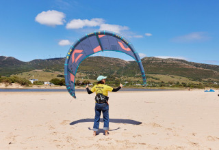 Istruttore fa volare un aquilone sulla spiaggia al TAIGA Tarifa Holiday Park, Andalusia, Spagna, con colline sullo sfondo.
