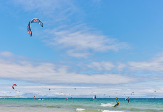 Kitesurfer gleiten über das Wasser im TAIGA Tarifa Ferienpark in Andalusien, Spanien an einem sonnigen Tag.