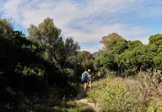 Two people walk along a lush trail in TAIGA Tarifa holiday park, surrounded by greenery in Andalusia, Spain.