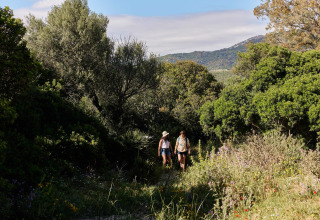 Zwei Menschen wandern auf einem Naturpfad inmitten grüner Vegetation im TAIGA Tarifa Ferienpark in Andalusien.