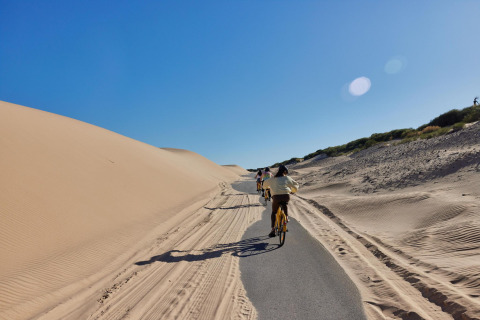 Cykelsti ved sandklitter under blå himmel i TAIGA Tarifa feriepark, Andalusien, Spanien.