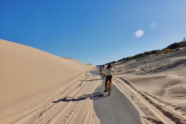 Fietspad langs zandduinen onder blauwe lucht bij TAIGA Tarifa vakantiepark, Andalusië, Spanje.