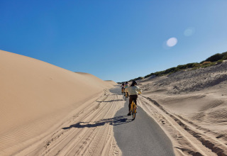 Cycling path beside sand dunes under blue sky at TAIGA Tarifa holiday park, Andalusia, Spain.