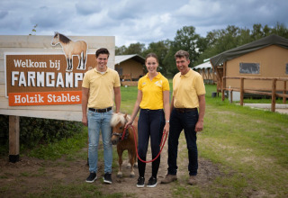 Drei Personen und ein Pony posieren vor dem FarmCamps-Holzik Stables Schild in Overijssel, Niederlande.