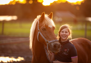 Meisje lachend met paard bij zonsondergang op FarmCamps Holzik Stables vakantiepark in Overijssel, Nederland.