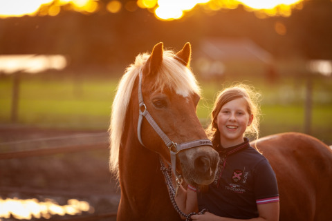 Ragazza che sorride accanto a un cavallo al tramonto presso FarmCamps Holzik Stables a Overijssel, Paesi Bassi.