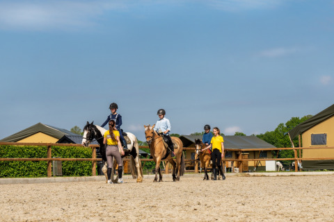 Kinderen krijgen paardrijles van instructeurs bij FarmCamps Holzik Stables vakantiepark in Overijssel.