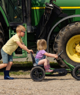 Dos niños juegan delante de un gran tractor verde en FarmCamps Holzik Stables en Overijssel, Países Bajos.