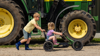 Dos niños juegan delante de un gran tractor verde en FarmCamps Holzik Stables en Overijssel, Países Bajos.