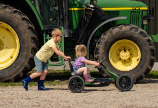 Dos niños juegan delante de un gran tractor verde en FarmCamps Holzik Stables en Overijssel, Países Bajos.