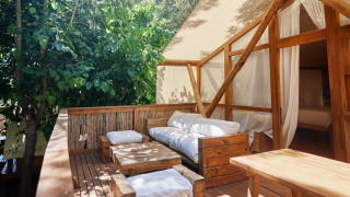 Terraza exterior con muebles de madera y cojines blancos en Glamping Luxury Tent La Cala, TAIGA Tarifa, España.