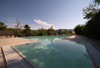 Infinity pool at Camping Podere Sei Poorte in Marche, Italy, surrounded by hills and lush nature under clear skies.
