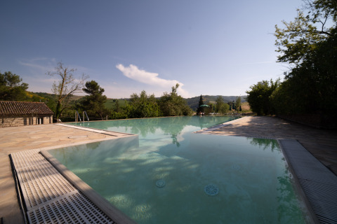Piscina infinita en Camping Podere Sei Poorte en Marche, Italia, rodeada de naturaleza y colinas verdes.
