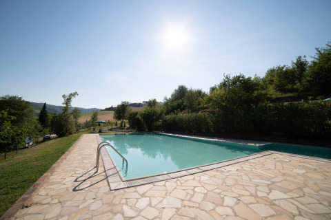 Piscina soleada en Camping Podere Sei Poorte, parque vacacional rodeado de naturaleza en Marche, Italia.
