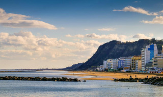 Vista de la playa y edificios cerca de Monteciccardo, Marche, Italia, con colinas al fondo y cielo azul.