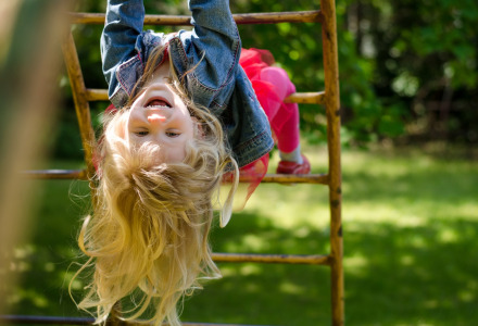 Niña sonriente cuelga boca abajo en un trepador cerca de Enschede, Overijssel, Países Bajos, momento alegre.