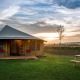 Safari-teltet Haytent står på en grøn græsplæne ved solnedgang, med træer og picnicbord i forgrunden.