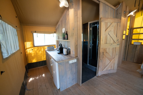 Indretning af Safari Lodge-telt med privat badeværelse, kitchenette og træinteriør på Camping Podere Sei Poorte.
