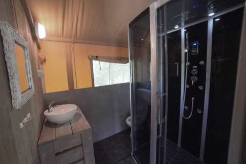 Bagno in tenda safari con doccia moderna, lavandino e finestra al Camping Podere Sei Poorte in Italia.