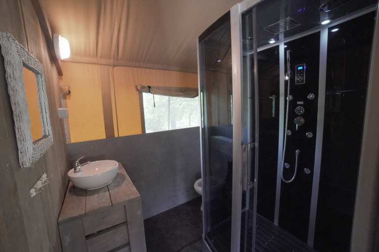 Baño de tienda safari con ducha moderna, lavabo y ventana en Camping Podere Sei Poorte en Italia.