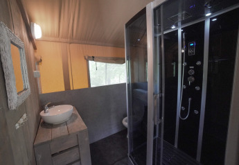 Bagno in tenda safari con doccia moderna, lavandino e finestra al Camping Podere Sei Poorte in Italia.
