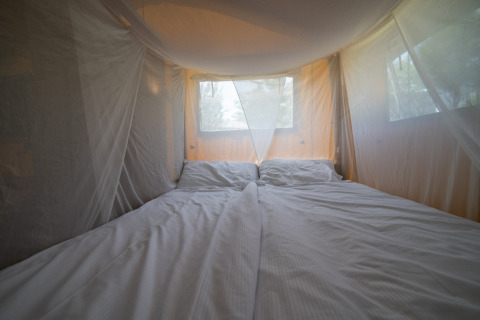 Vista interior de tienda safari con cama doble y mosquitera en Camping Podere Sei Poorte en Italia.