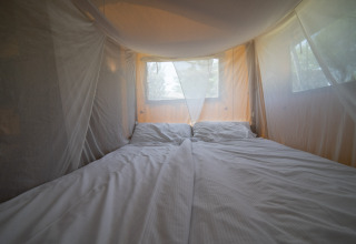 Vista interior de tienda safari con cama doble y mosquitera en Camping Podere Sei Poorte en Italia.