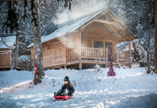 Kinder spielen im Schnee vor einer Holzhütte im Les Chalets Huttopia de Bozel, Auvergne-Rhône-Alpes, Frankreich.