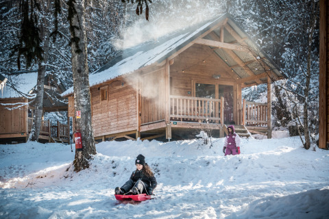Kinderen spelen in de sneeuw bij een houten chalet in Les Chalets Huttopia de Bozel, Auvergne-Rhône-Alpes, Frankrijk.