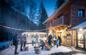 Mensen rond een kampvuur in de sneeuw voor een houten chalet bij Les Chalets Huttopia de Bozel.