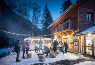 Menschen genießen ein winterliches Lagerfeuer vor einer Holzhütte in Les Chalets Huttopia de Bozel.