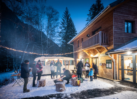 Personas disfrutan de una fogata invernal en la nieve frente a una cabaña en Les Chalets Huttopia de Bozel.