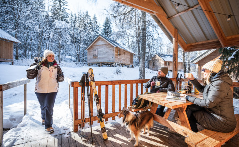 Winter bij Les Chalets Huttopia de Bozel, mensen genieten van warme dranken en een besneeuwd landschap.