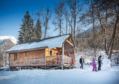 Gezin maakt een sneeuwpop bij een houten chalet in Les Chalets Huttopia de Bozel, in besneeuwd Frankrijk.