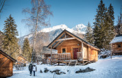 Houten chalet in besneeuwde bergen bij Chalet Montana, Les Chalets Huttopia de Bozel, Frankrijk, blauwe lucht.