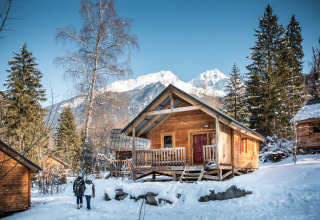 Blockhütte im Schnee bei Chalet Montana, Les Chalets Huttopia de Bozel, Frankreich, mit Bergen im Hintergrund.