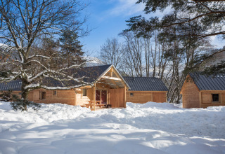 Cabañas de madera en Les chalets Huttopia de Bourg-St-Maurice, Francia, rodeadas de nieve y árboles en invierno.