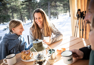 Familie genießt Frühstück und heiße Getränke in einer Holzhütte im Schnee in Südfrankreich.