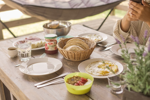 Ontbijttafel bij Camping Les Sapins in Occitanië, Frankrijk, met brood, eieren, confituur en koffie.
