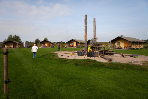 Familias disfrutan de actividades al aire libre y el área de juegos en FarmCamps Hoeve Sonneclaer en Drenthe, Países Bajos.