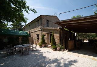 Outdoor dining and rustic stone building at Camping Podere Sei Poorte, Marche, Italy on a sunny day.