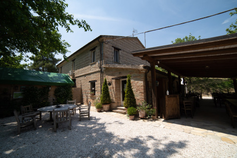 Comedor al aire libre y edificio de piedra en Camping Podere Sei Poorte, Marche, Italia, día soleado.