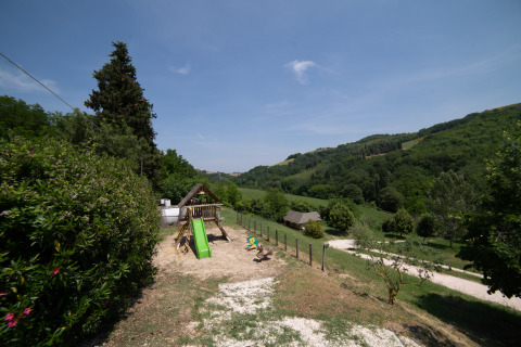 Parque infantil con tobogán en Camping Podere Sei Poorte, rodeado de colinas verdes en Marche, Italia.