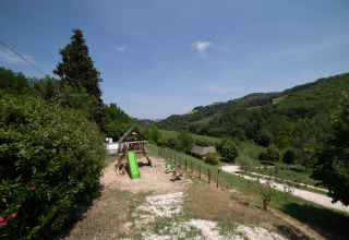 Parco giochi con scivolo al Camping Podere Sei Poorte, circondato da colline verdi nelle Marche, Italia.