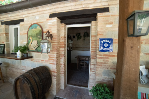 Entrada a un restaurante rústico con paredes de ladrillo y barril en Camping Podere Sei Poorte, Marche, Italia.