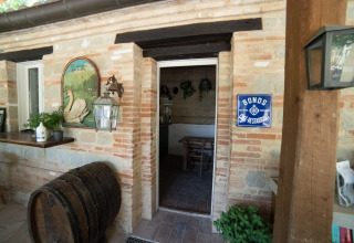 Ingang van een restaurant met bakstenen muren en wijnvat op Camping Podere Sei Poorte in Marche, Italië.
