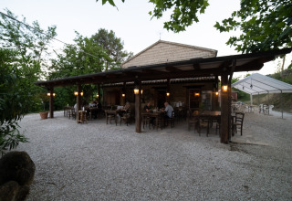 Outdoor dining area at Camping Podere Sei Poorte holiday park in Marche, Italy, surrounded by greenery.