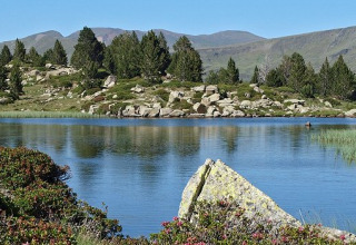 Panoramabillede af en fredelig sø omgivet af fyrretræer og klipper ved Camping Les Sapins i Occitanie, Frankrig.